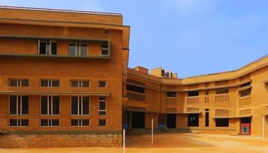 A modern school building constructed with vintage-style brown bricks, exuding timeless charm. The structure is surrounded by lush greenery, creating a serene atmosphere.