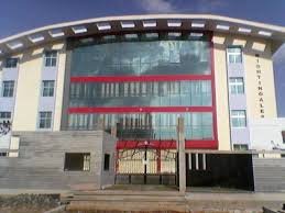 A large, modern school building with yellowish hues, featuring large glass windows, and a spacious, welcoming entrance.